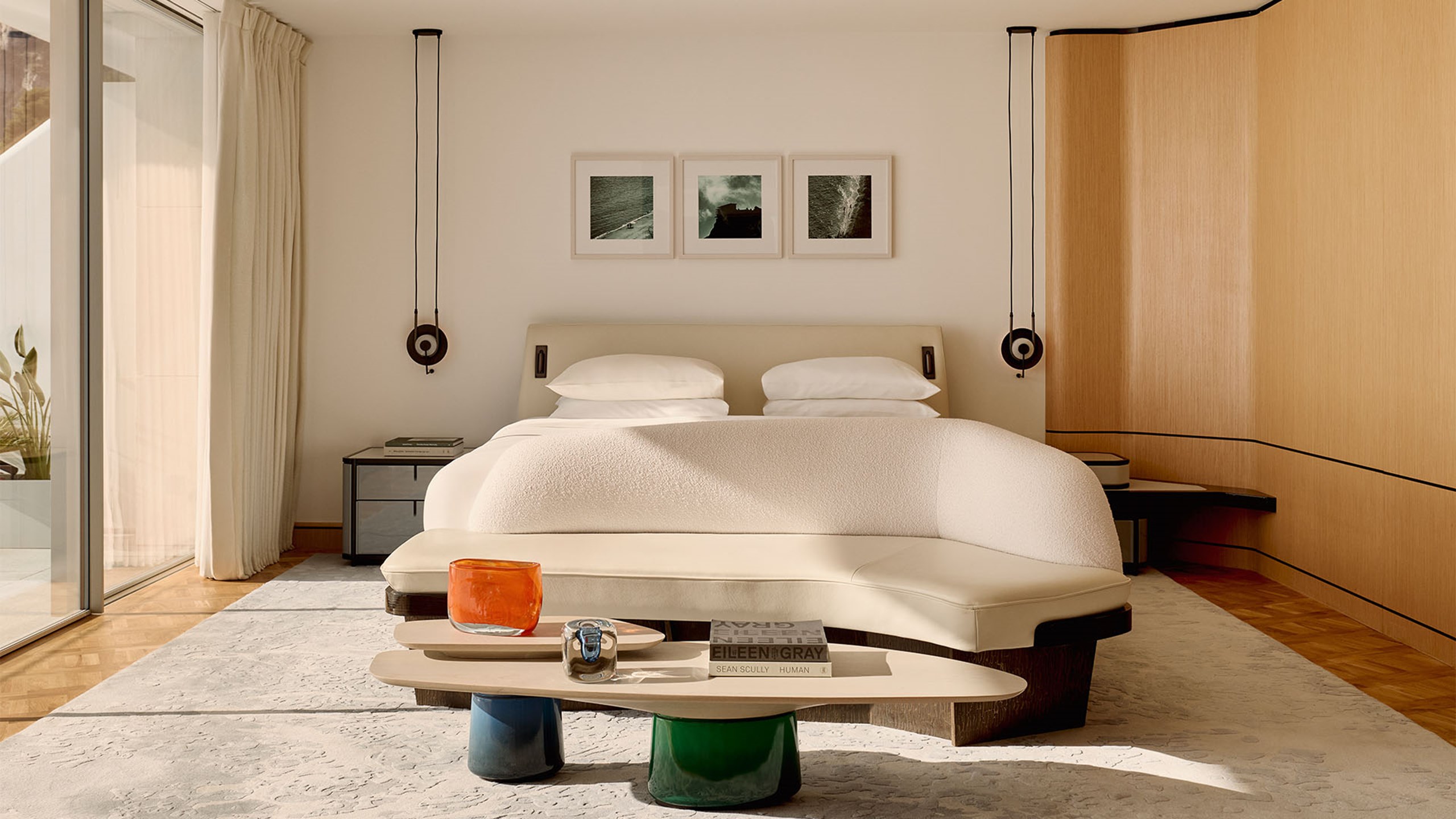 Elegant bedroom with a double bed, soft cream tones, modern bench seating, and three framed photographs above the headboard.