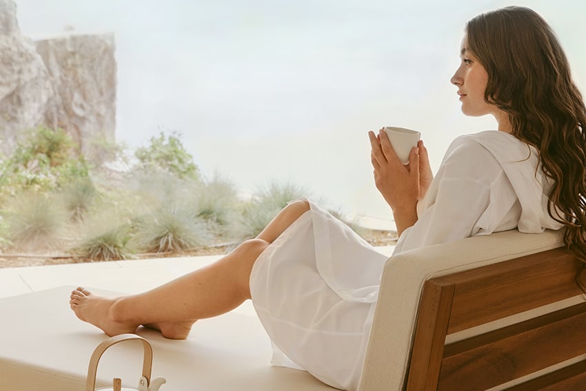 Brown-haired woman holding a cup of tea at The Maybourne Riviera Spa and enjoying the view.