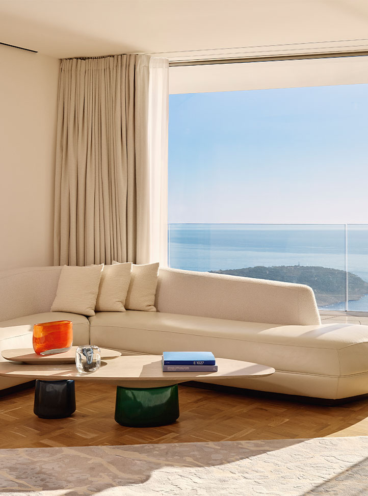 Minimalist living room with cream corner sofa, low coffee table, and floor-to-ceiling window offering panoramic ocean views.